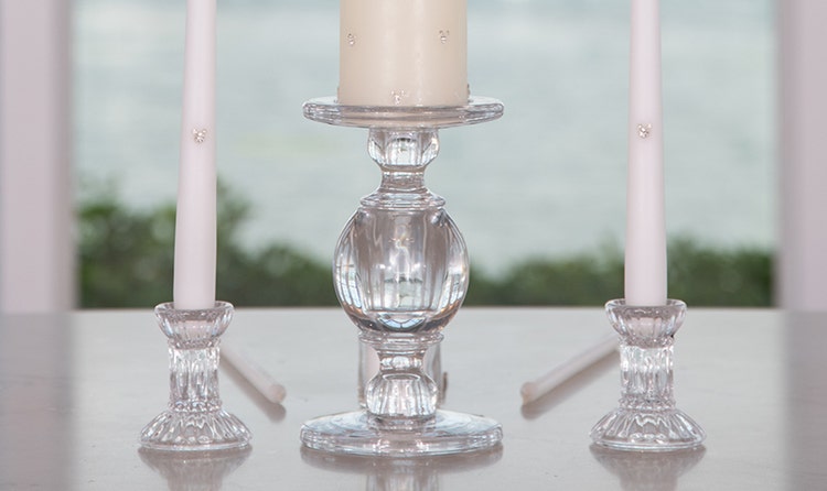 Three candles on glass holders on a table, with a large pillar candle in the center and 2 taper candles on either side