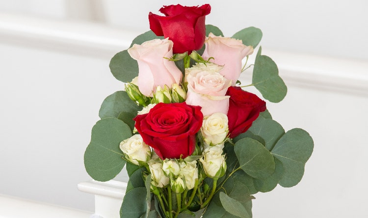 Floral arrangement of roses with greenery tied to a white pew
