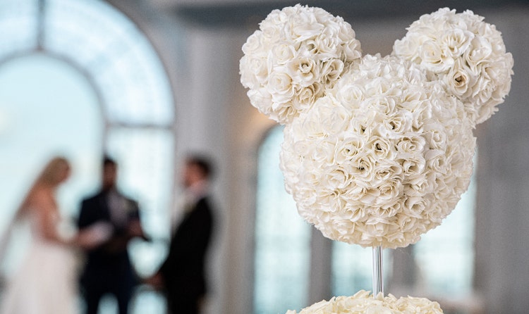 Floral arrangement of roses shaped like Mickey Mouse and a couple in the background during a ceremony