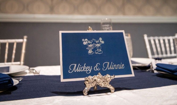 Table setup featuring a card with 'Mickey & Minnie' text and silhouettes of Mickey and Minnie projected on the wall