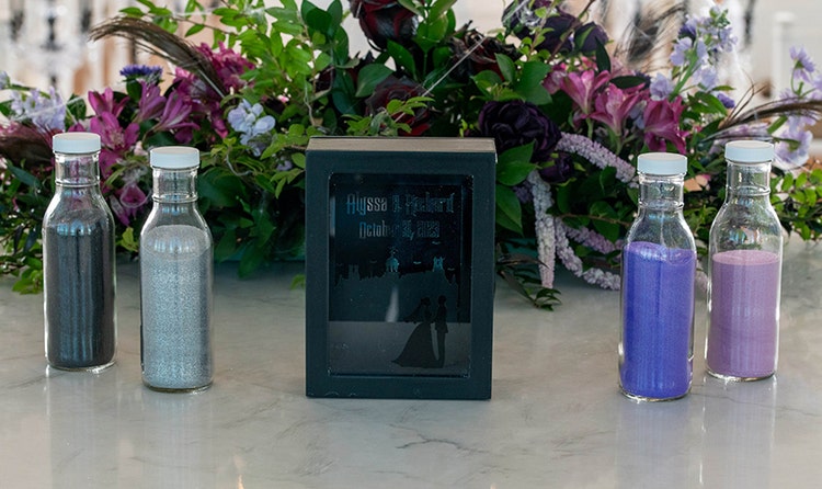 Sand ceremony setup with 4 bottles of sand, a frame displaying a Halloween themed invitation and a floral arrangement