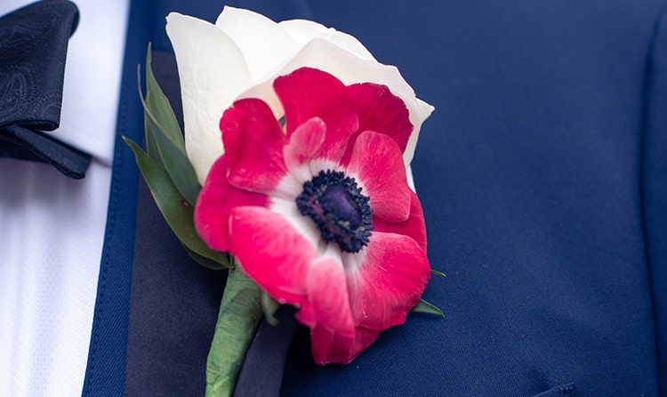 A groom wearing a boutonniere with a mix of a rose and another flower