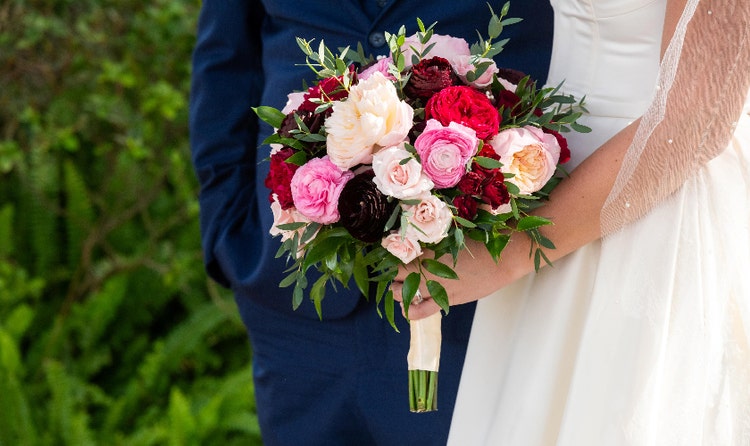 A bride holding a bouquet with roses and ranunculuses