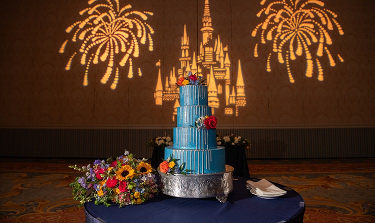 Wedding cake with a Castle topper, intricate filigree designs and a beaded pattern, set on a table in a grand venue