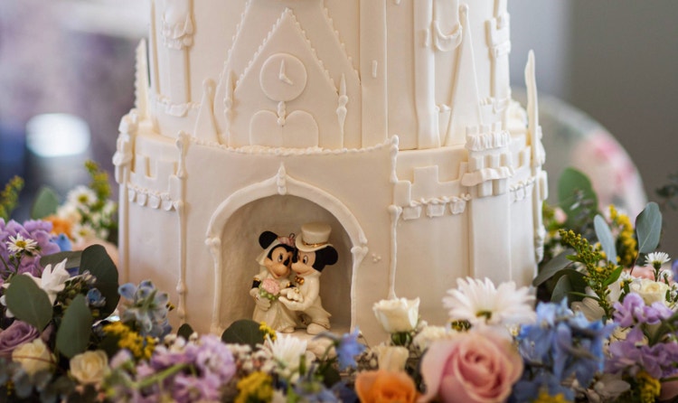 A grand, multi tiered wedding cake designed like a castle featuring an arch with Mickey and Minnie figurines and a floral base