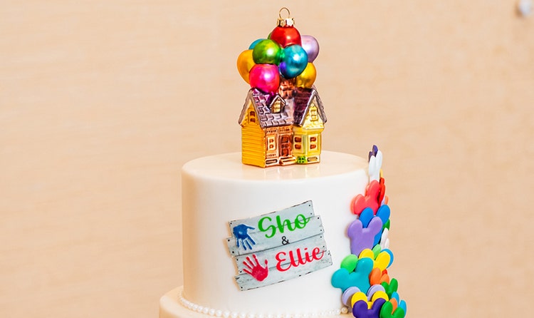 Wedding cake featuring a house topper with balloons inspired by the movie Up, a 'Sho & Ellie' sign and cascading Mickey shaped accents