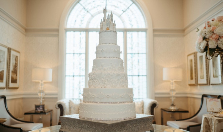 A grand, multi tiered wedding cake with a castle topper, beaded trim and frosting roses in an elegant room