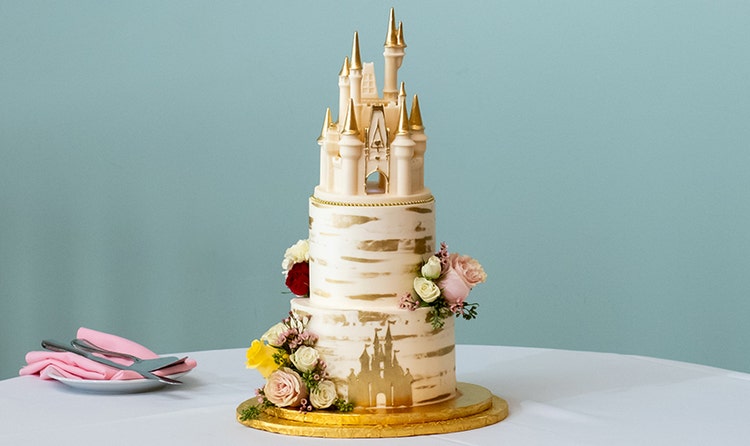 Wedding cake with a Cinderella Castle topper, floral decorations and a painted design featuring a castle silhouette