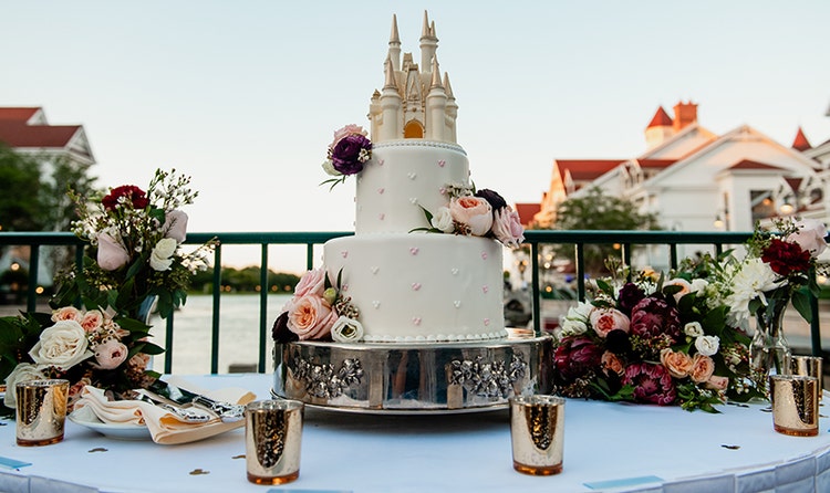 Wedding cake with a Cinderella Castle topper, floral decorations and small heart accents alongside flower bouquets and tea lights