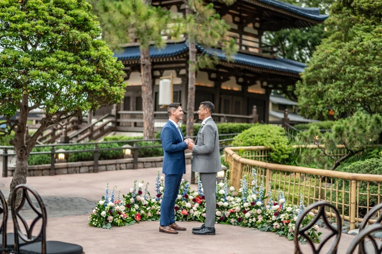 Two men are all smiles as they hold hands and look into each other’s eyes near a bamboo fence in the EPCOT Japan Pavilion at Walt Disney World Resort